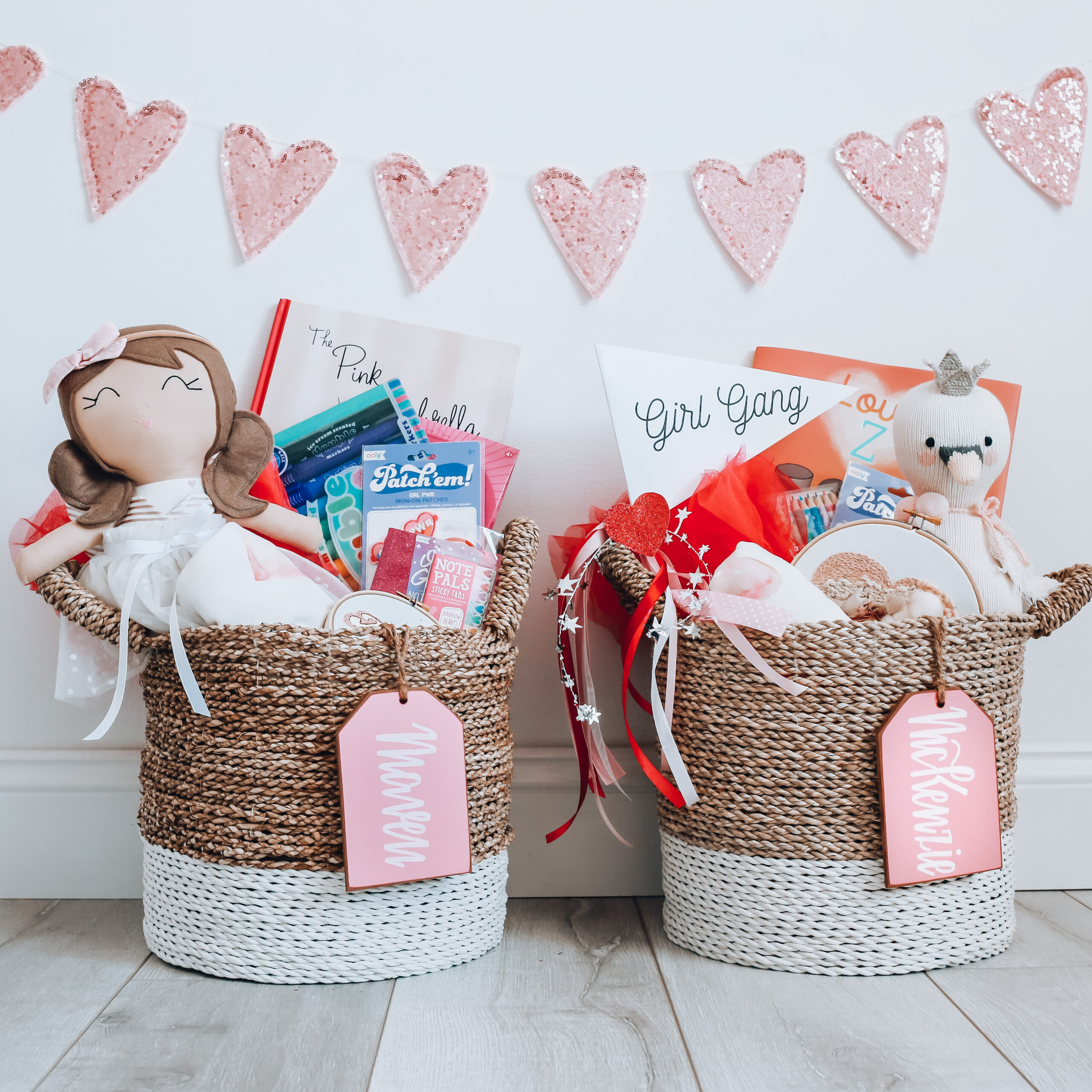 Two seagrass baskets with doll, stuffed animal and Valentine candy with two pink name tags.
