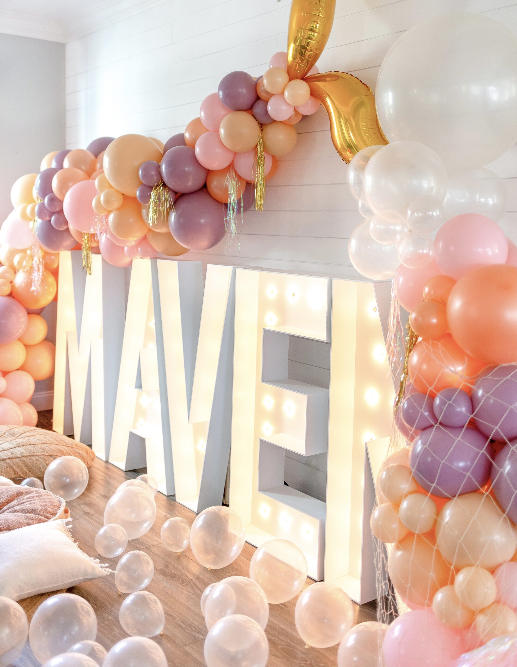 Maven in light up letters with purple, pink, peach and cream balloons in the shape of a mermaid tail