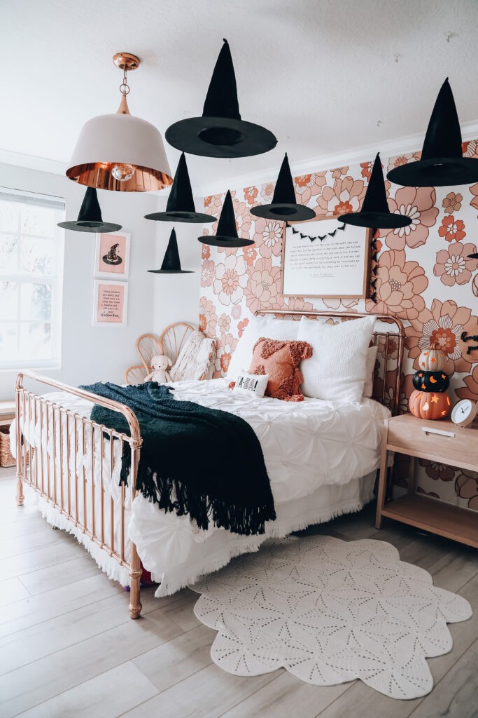 Black witch hats hanging in girls bedroom with floral wallpaper